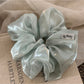 Close-up of a minimalist satin ruched scrunchie in soft beige on a white background