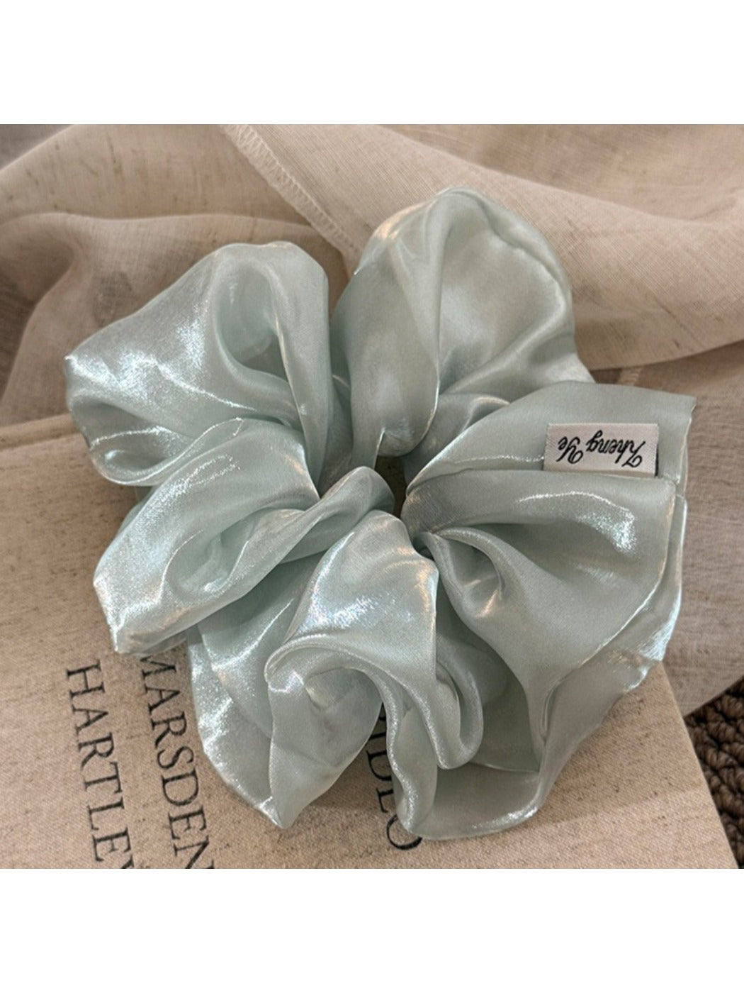 Close-up of a minimalist satin ruched scrunchie in soft beige on a white background