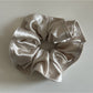 Gifty satin scrunchie held between fingers showing elasticity and fabric quality