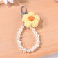 Yarn flower keychain with beads displayed alongside keys on a wooden table