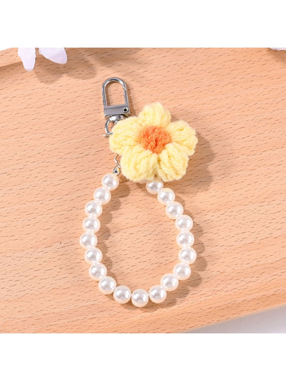 Yarn flower keychain with beads displayed alongside keys on a wooden table