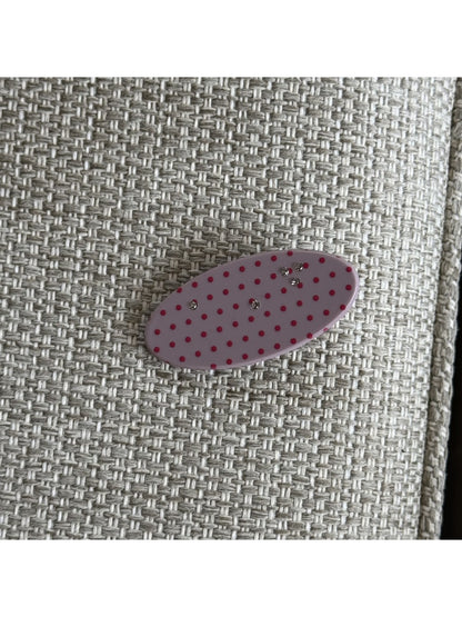 Beau pink polka dot claw clip resting on a white surface with soft lighting