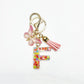 Silver keychain with butterfly and letter pendant against a pastel background