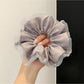 Hand holding a pink satin ruched scrunchie against a white background