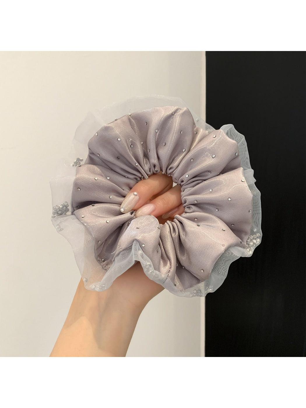 Hand holding a pink satin ruched scrunchie against a white background