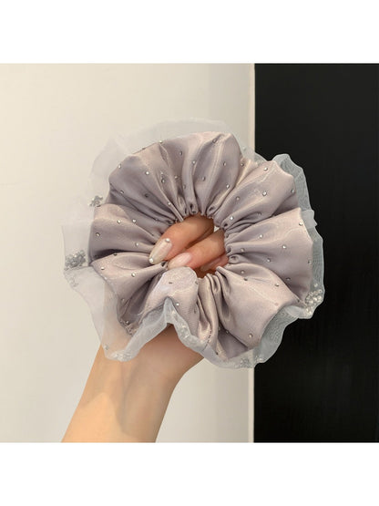 Hand holding a pink satin ruched scrunchie against a white background