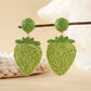 Raffia strawberry earrings placed on natural wood surface