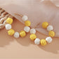 Pair of Earedge raffia round ball drop earrings laid flat on wooden surface