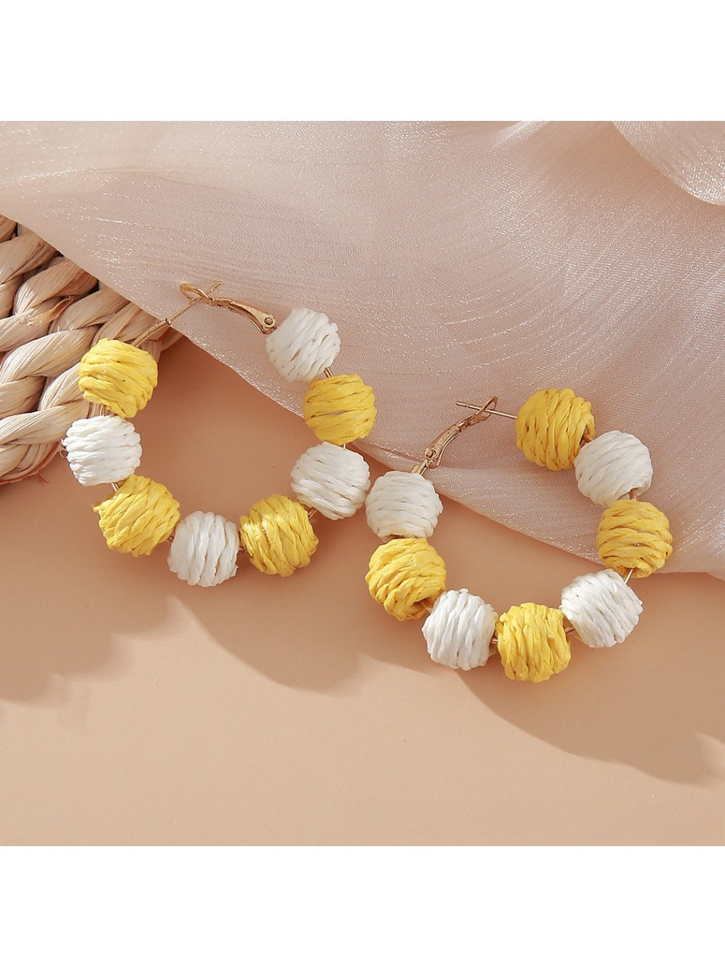 Pair of Earedge raffia round ball drop earrings laid flat on wooden surface