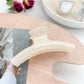 Pastel curved claw clip photographed with soft shadows on white surface
