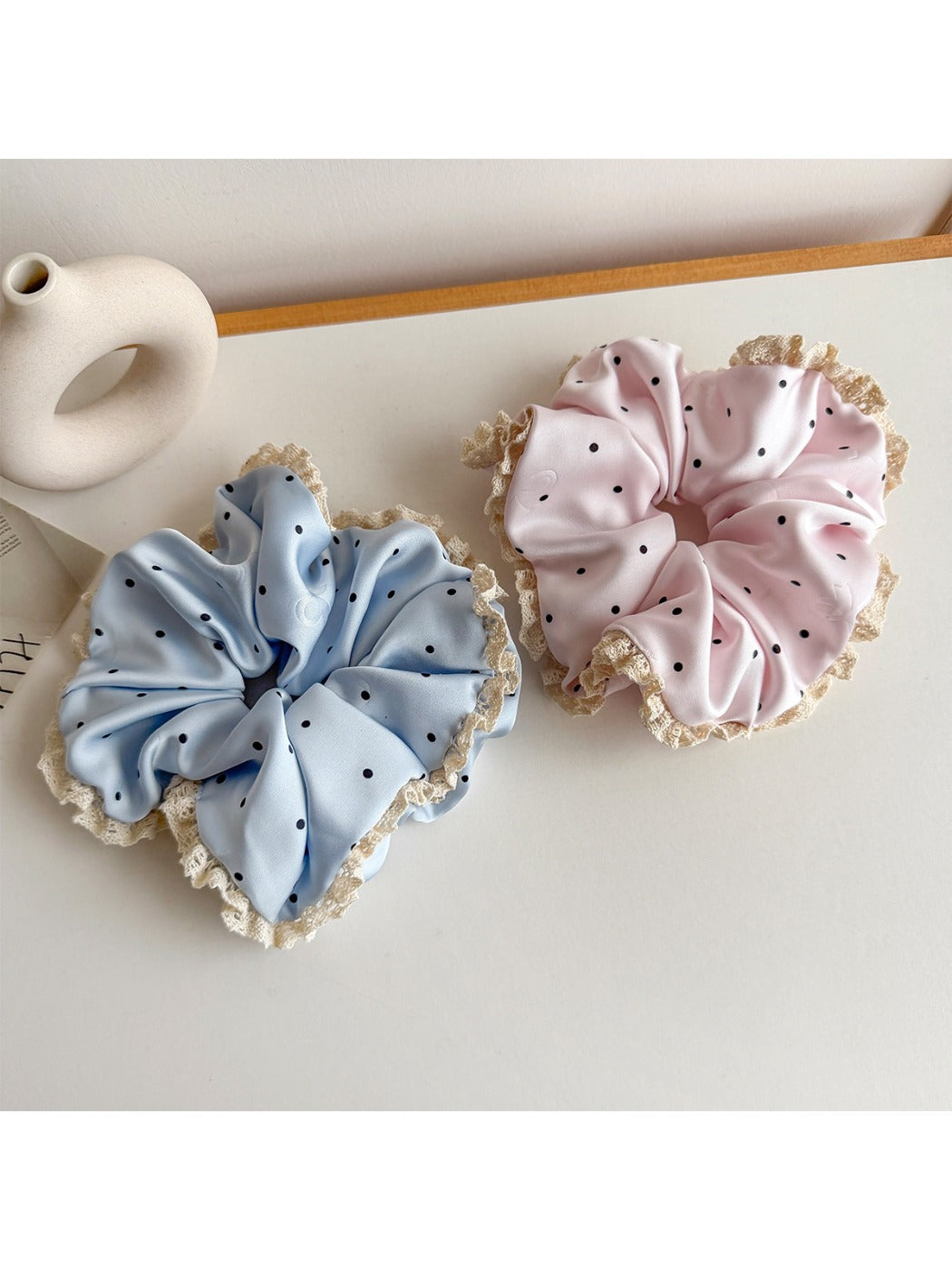 Gifty scrunchie with white polka dots and delicate lace trim on a neutral background