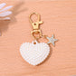 Heart shaped bag charm keychain attached to a set of keys on a white background