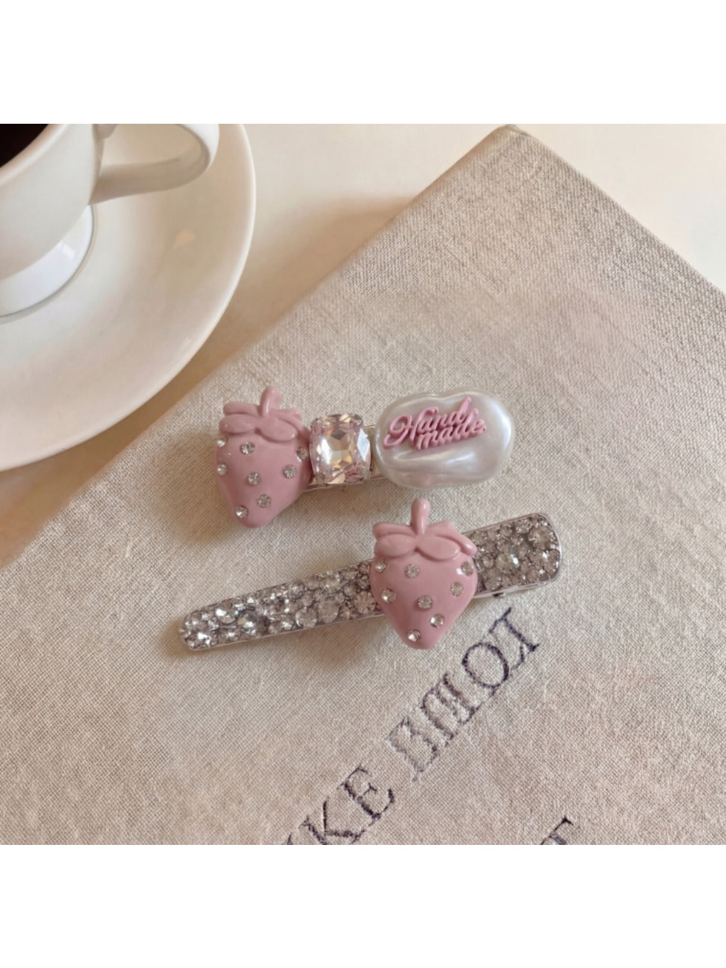 Beau hair clip held in hand showing size and strawberry decoration with green leaf accents