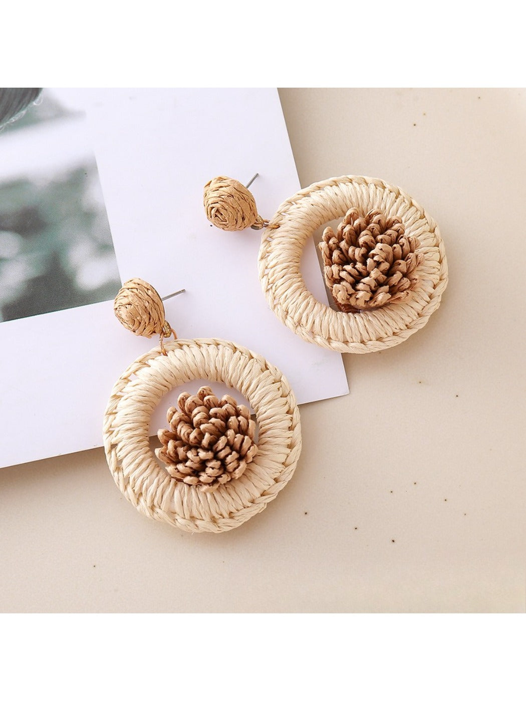 Pair of Earedge creative raffia earrings hanging from a jewelry stand