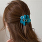 Side view of beige flower shaped claw clip with metal spring visible