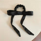 Close-up of a satin bow embellished hair tie in soft pink on a white background