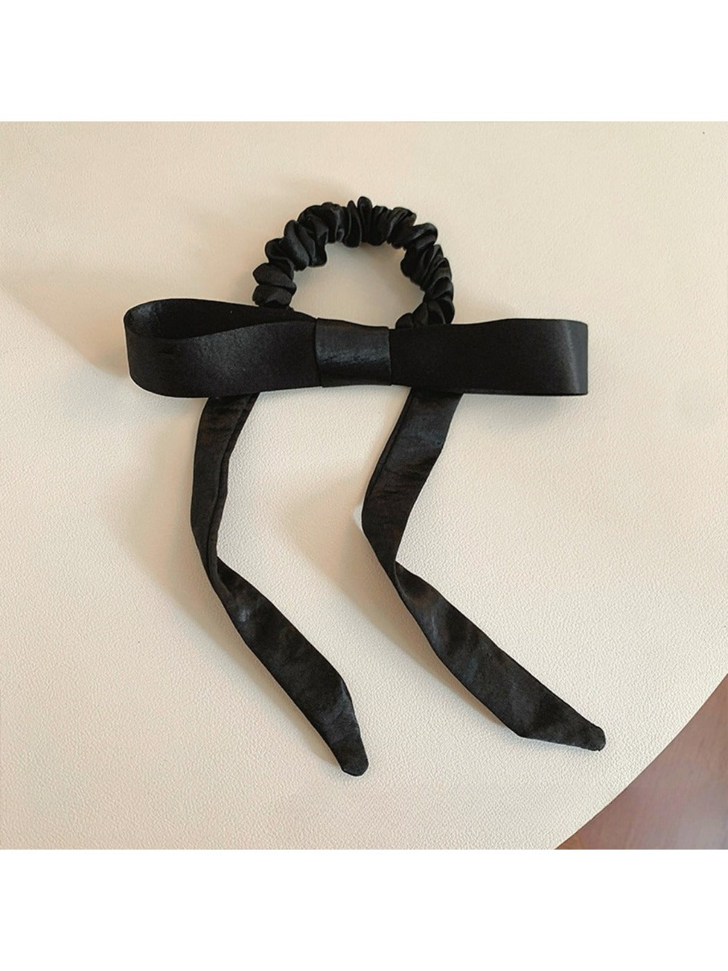 Close-up of a satin bow embellished hair tie in soft pink on a white background