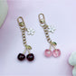 Close-up of a stylish cherry charm keychain with red enamel cherries and green leaves