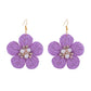 Earedge raffia flower earrings hanging on a jewelry stand with soft lighting