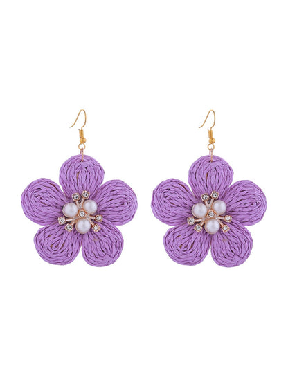 Earedge raffia flower earrings hanging on a jewelry stand with soft lighting