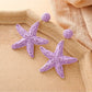 Silver starfish drop earrings placed on a natural seashell