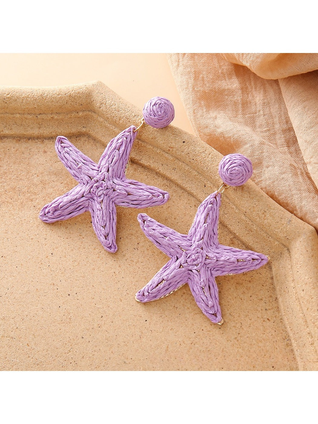 Silver starfish drop earrings placed on a natural seashell