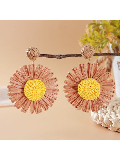 Vintage sunflower earrings hanging from a branch with green leaves