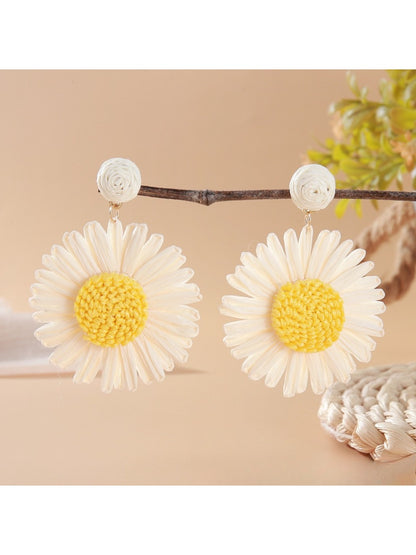 Raffia woven sunflower earrings resting on a wooden surface with natural light
