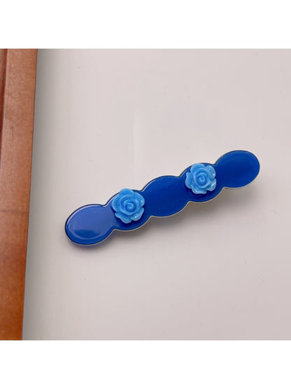 Beau hair clip with pink rose decoration placed next to flowers