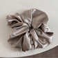 Glossy satin scrunchie in pink held between fingers showing size