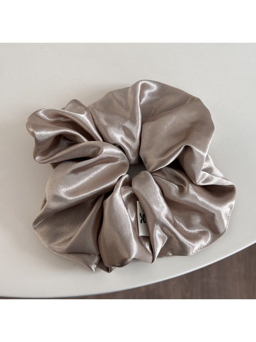 Glossy satin scrunchie in pink held between fingers showing size