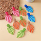 Close-up of Earedge raffia woven leaf shaped earrings on white background