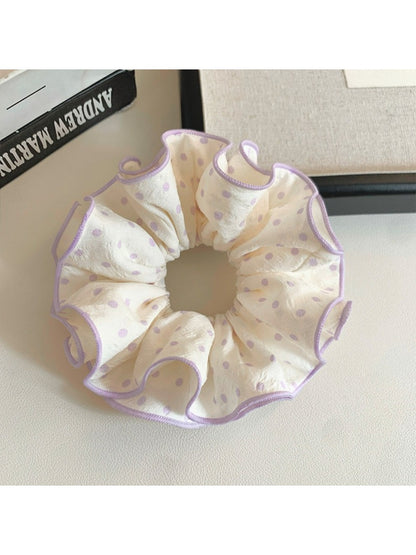 Close-up of purple fabric scrunchie featuring white polka dots