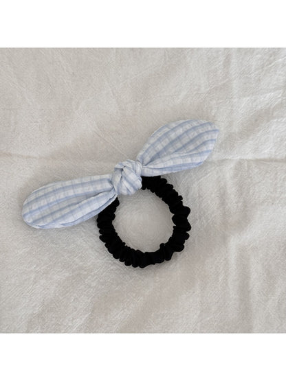 Gifty hair tie with red bow and plaid design held in hand against a neutral background