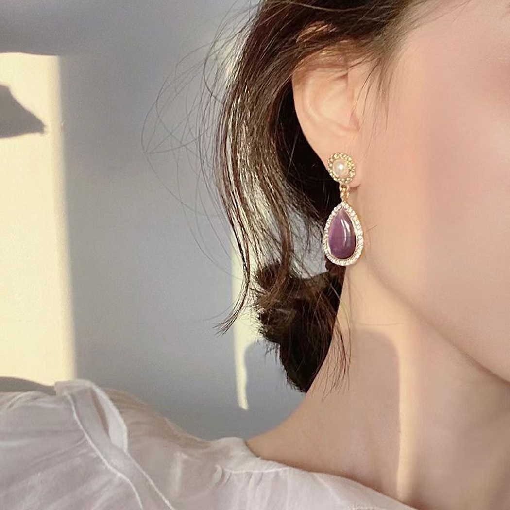 Purple teardrop earring worn beside short dark hair in sunlight