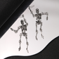 Silver-colored skeleton earrings arranged on a curved mirror with reflections beneath the figures
