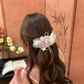 Purple floral hair claw with layered flowers and ribbon loops on a low ponytail