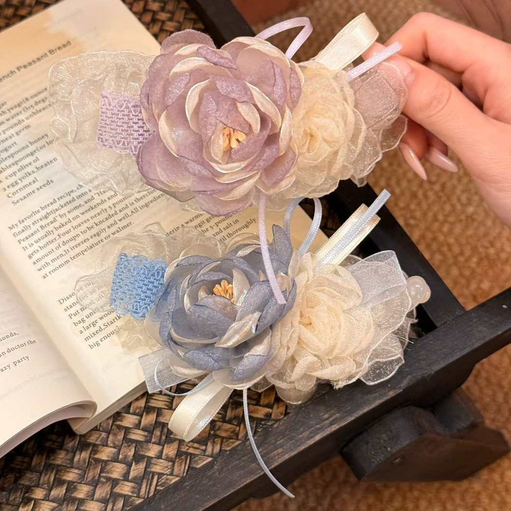 Blue and purple floral hair claws with layered flowers and hanging ribbons, handheld front view