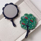 Mirroray handheld mirror with tree-shaped frame next to decorative items