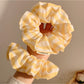 Yellow scrunchie with thin white stripes on a plain background