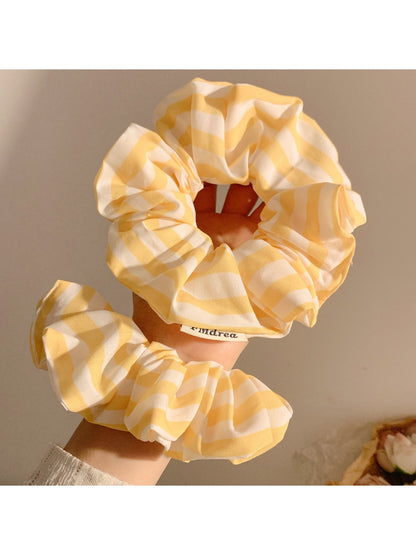 Yellow scrunchie with thin white stripes on a plain background
