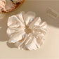 Close-up of minimalist satin scrunchie with bow pattern on white background