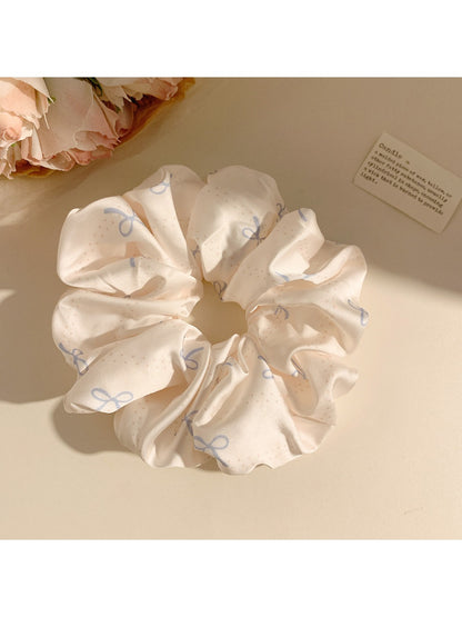 Close-up of minimalist satin scrunchie with bow pattern on white background