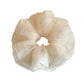 Beige tulle scrunchie wrapped around a ponytail in soft natural light