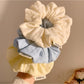 Multiple Gifty scrunchies in different solid colors with floral prints displayed on a white background