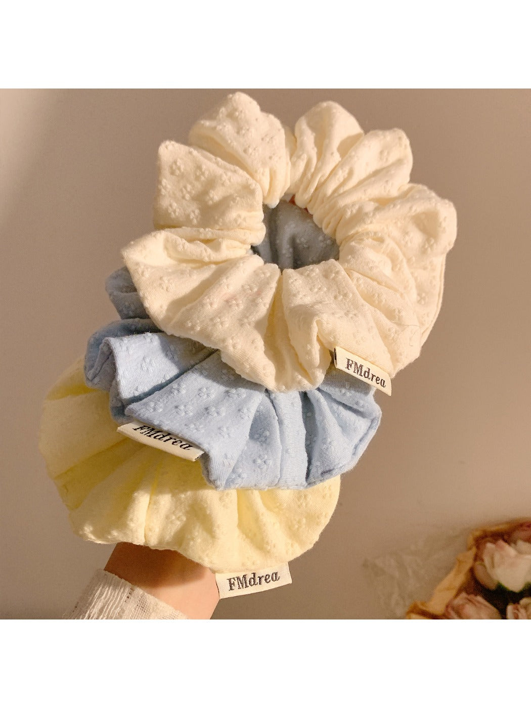 Multiple Gifty scrunchies in different solid colors with floral prints displayed on a white background