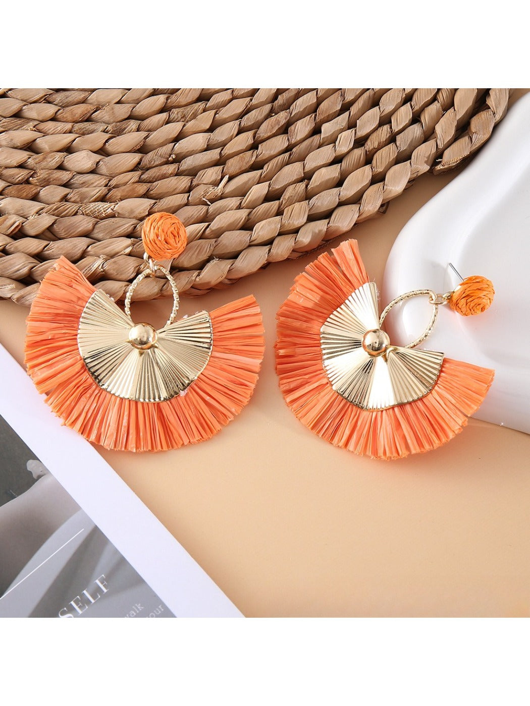 Earedge raffia fan earrings displayed with green leaves in background