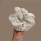 Beige tulle scrunchie with white polka dots wrapped around a ponytail in brown hair