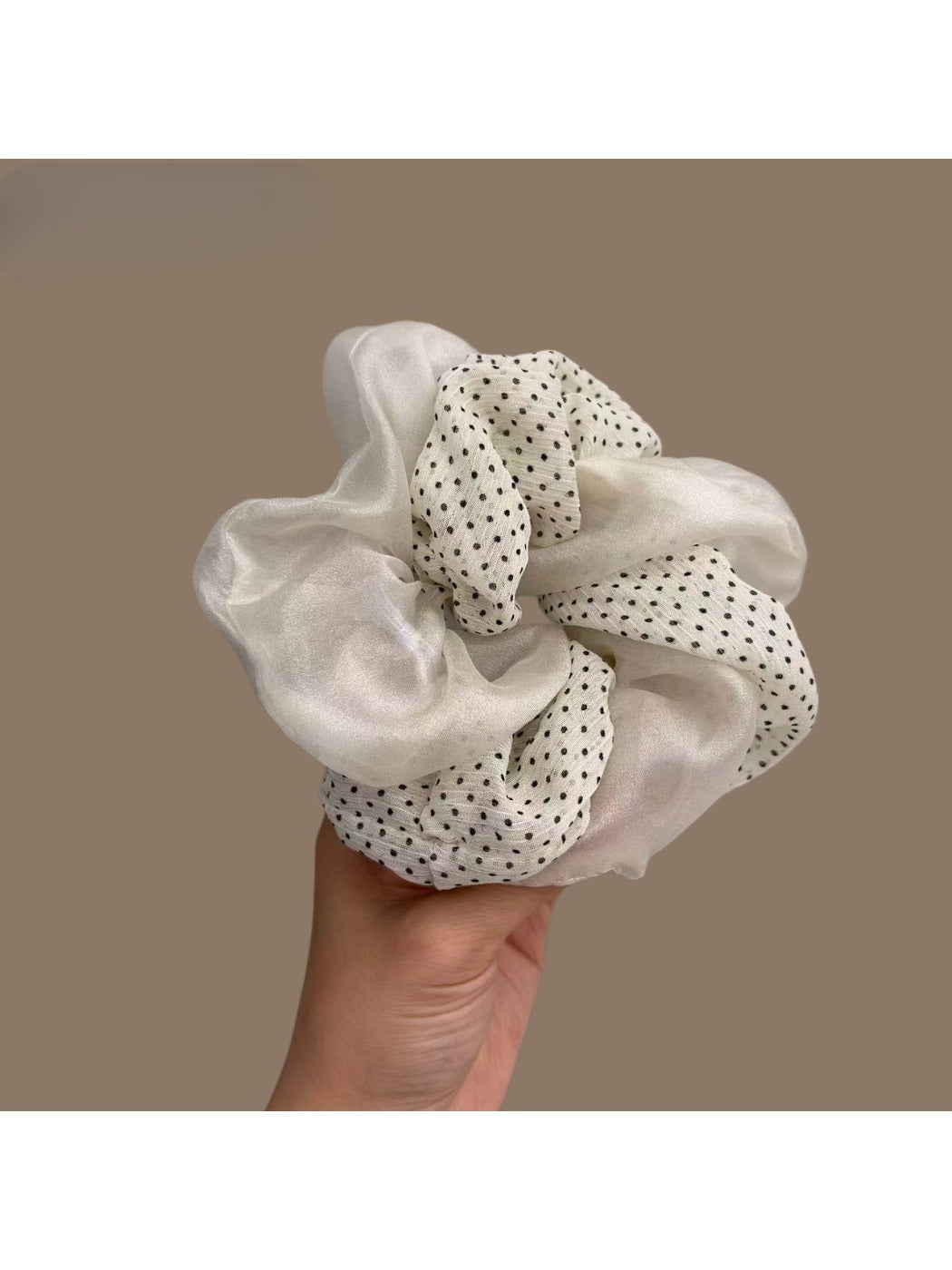 Beige tulle scrunchie with white polka dots wrapped around a ponytail in brown hair