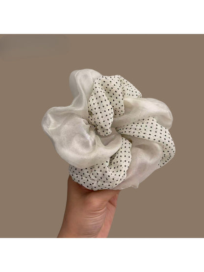 Beige tulle scrunchie with white polka dots wrapped around a ponytail in brown hair